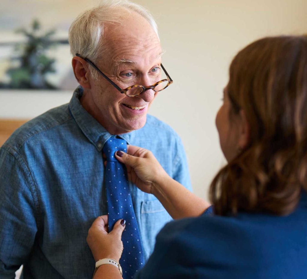 Assistant tying a tie on a resident