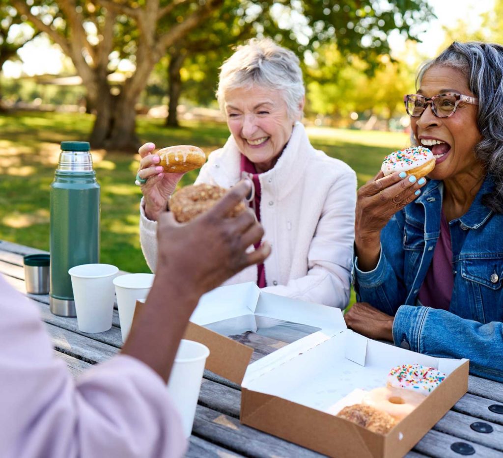 Smiling senior women eating donuts outdoor